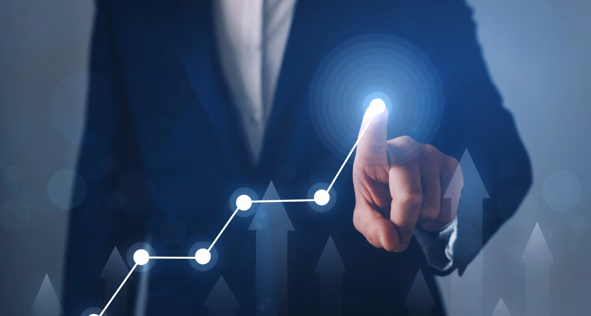 A person in a suit pointing at a line on a graph going up