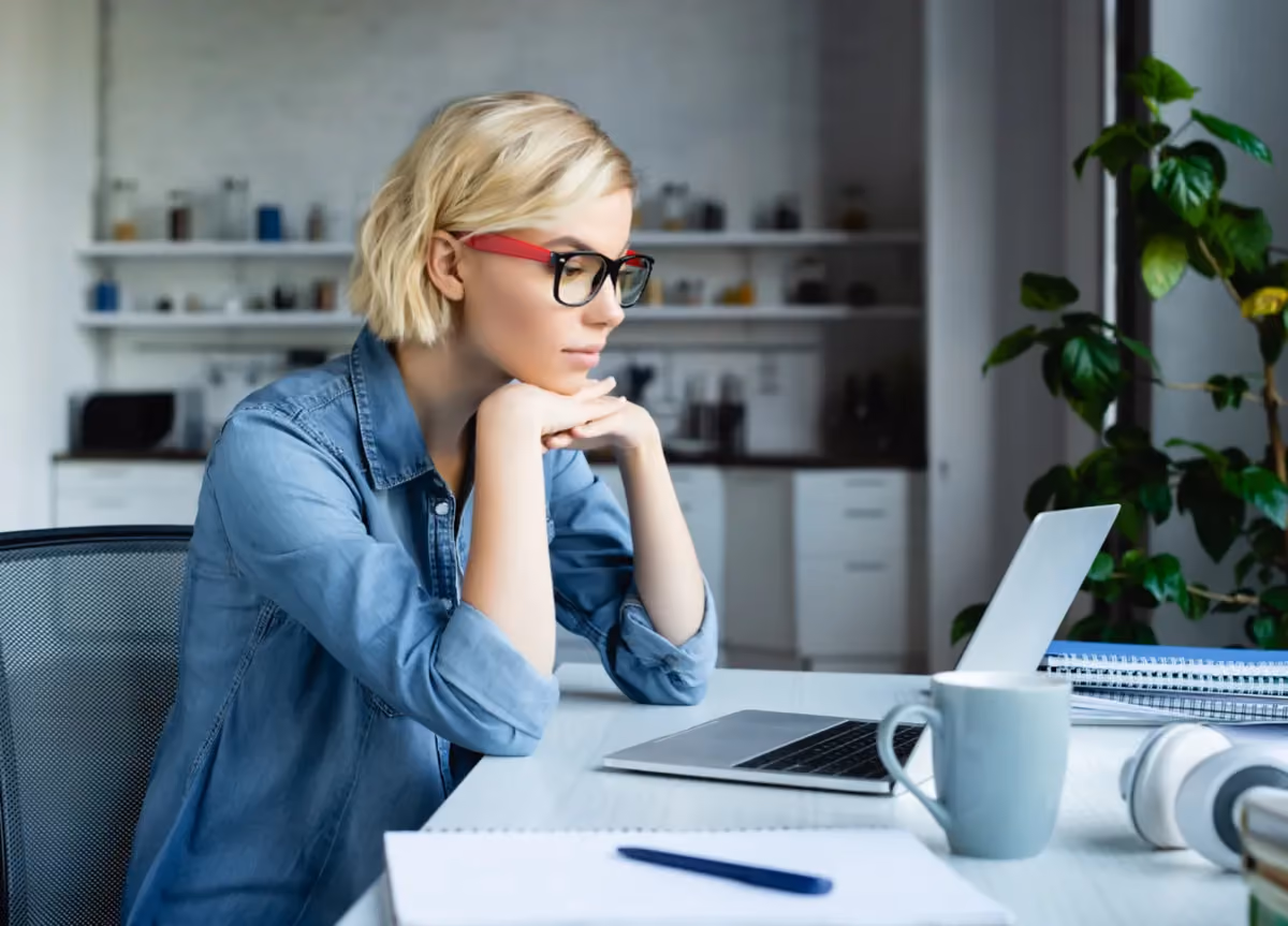 Concentrated blonde woman wearing eyeglasses working on her laptop