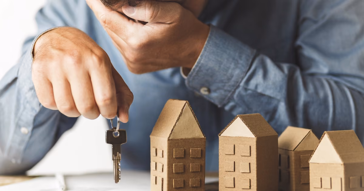A man holding a set of keys looking down at a set of model houses