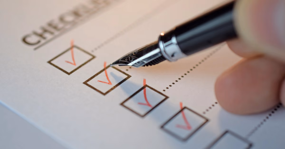 A hand holding a pen, ticking a box on a checklist