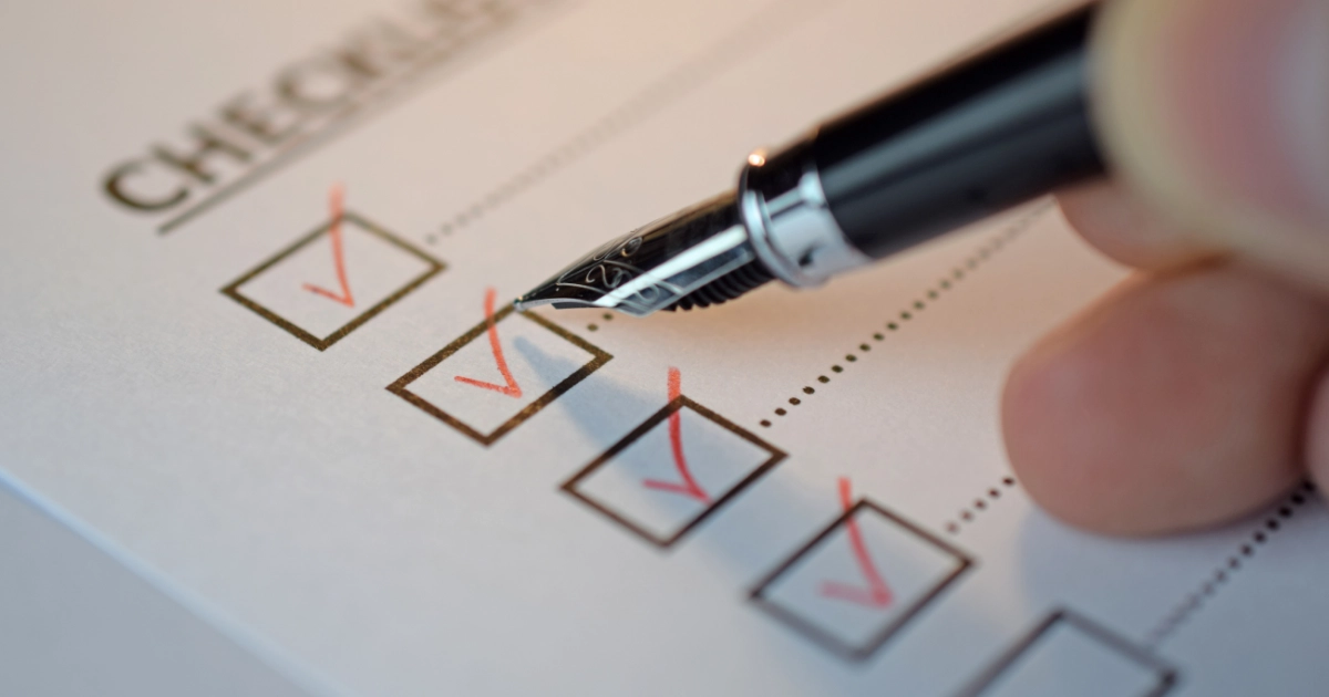 A hand holding a pen, ticking a box on a checklist