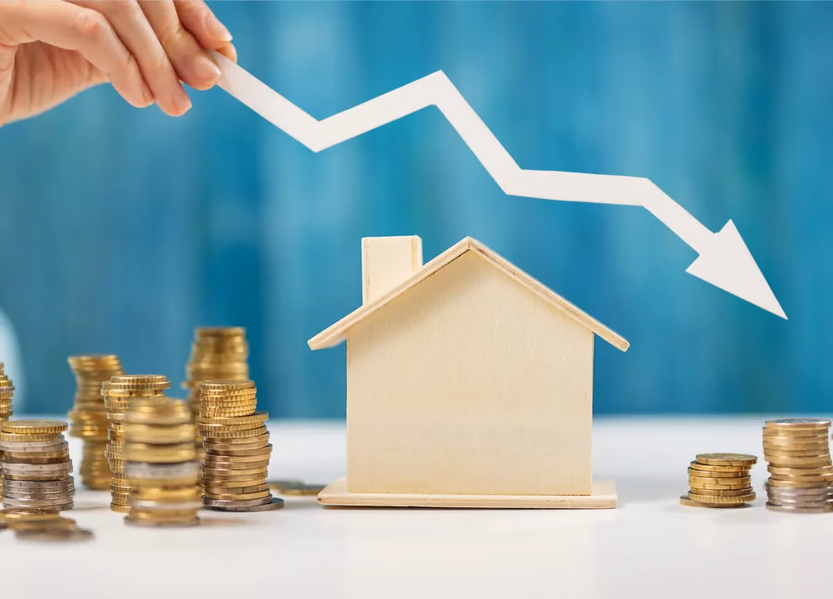 Woman holds an arrow down over model of a house and stack of coins.