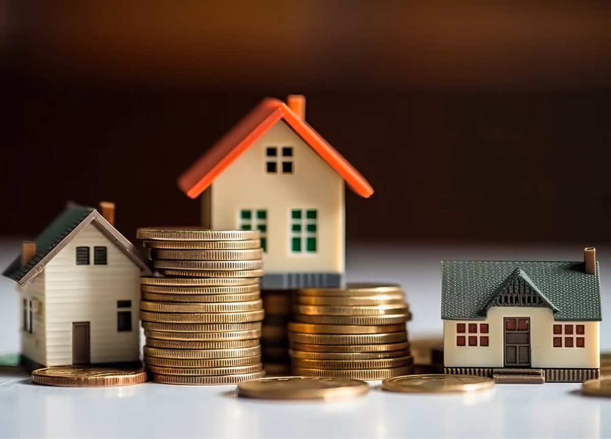 Three small model houses perched on different-sized heaps of golden coins