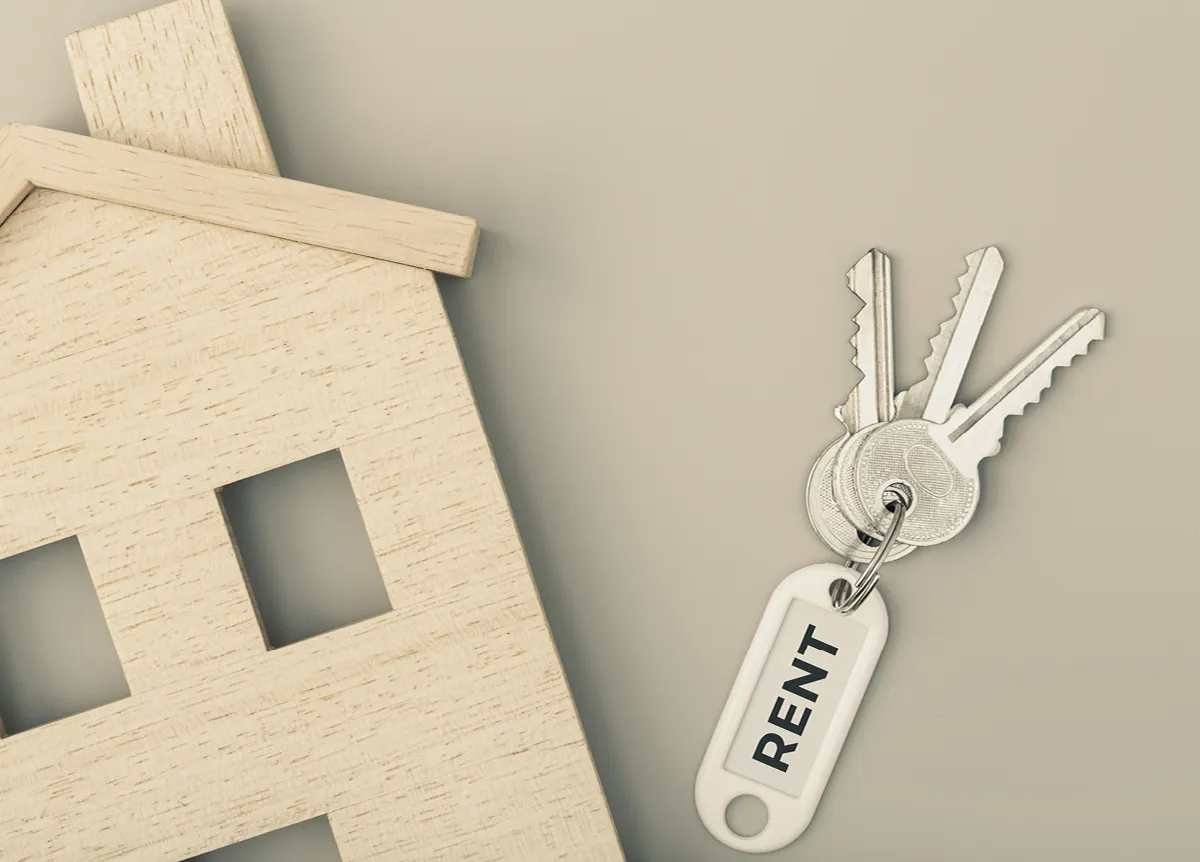 Set of keys with a "rent" keychain next to wooden model house
