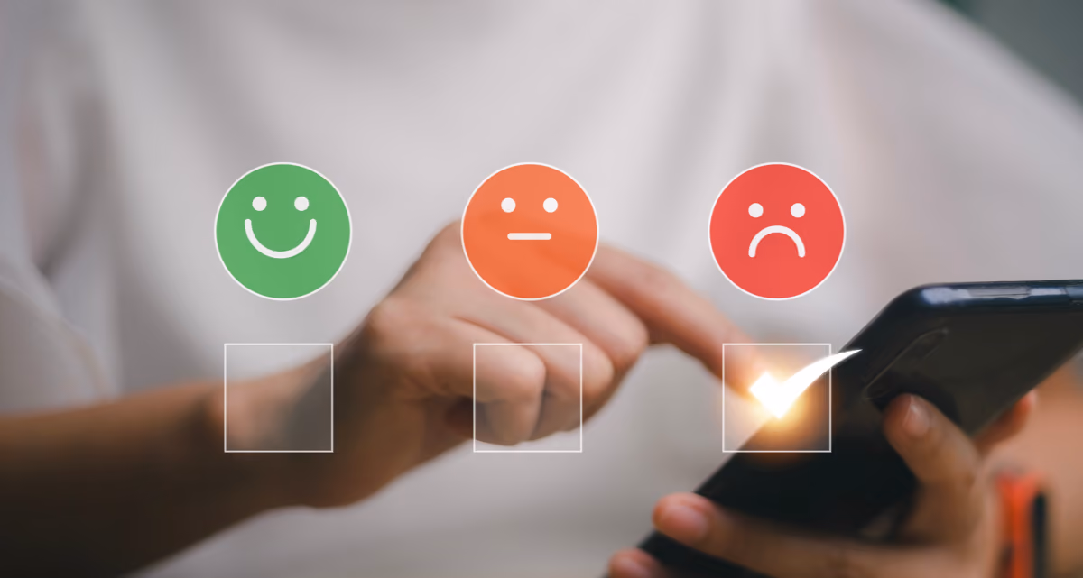 A closeup of a person tapping their smartphone screen with a green smiley face, an orange neutral face and a red frowning face over it