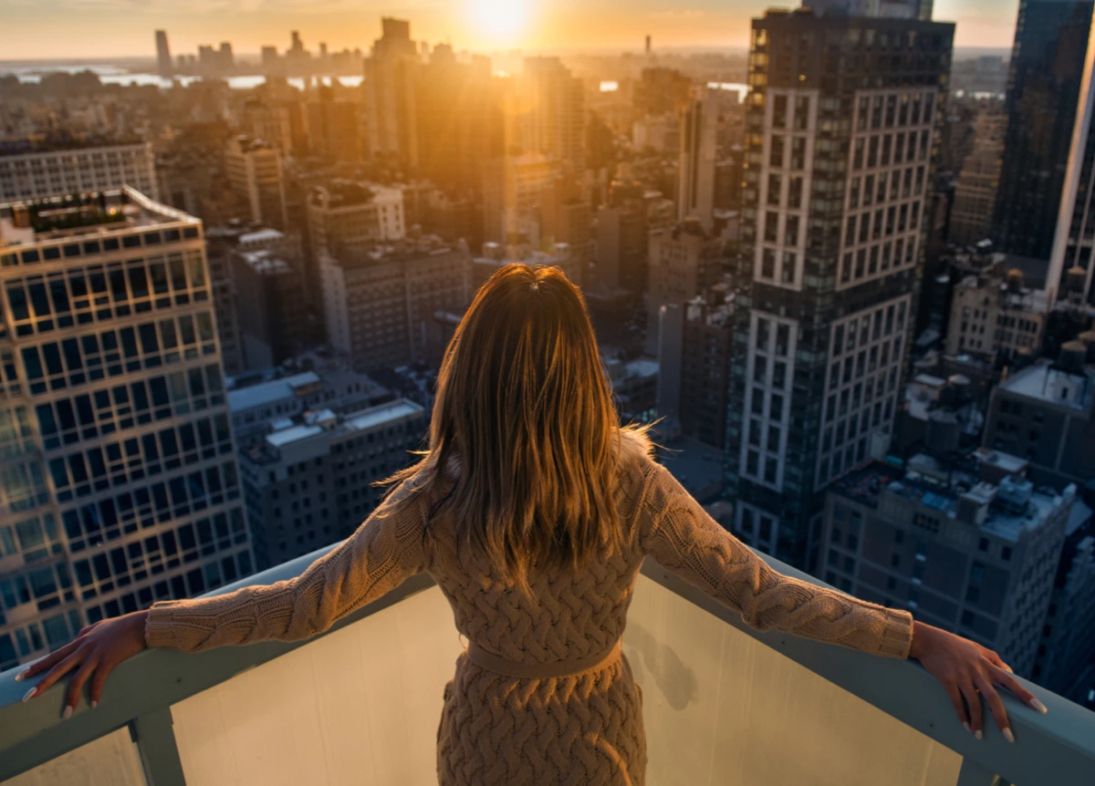 Blonde woman standing on balcony, overlooking a city