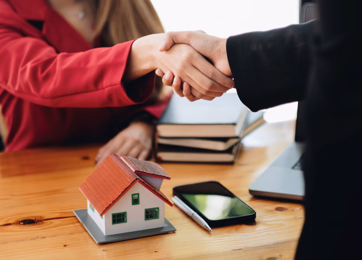 Man and woman shake hands above a model of a single-family home