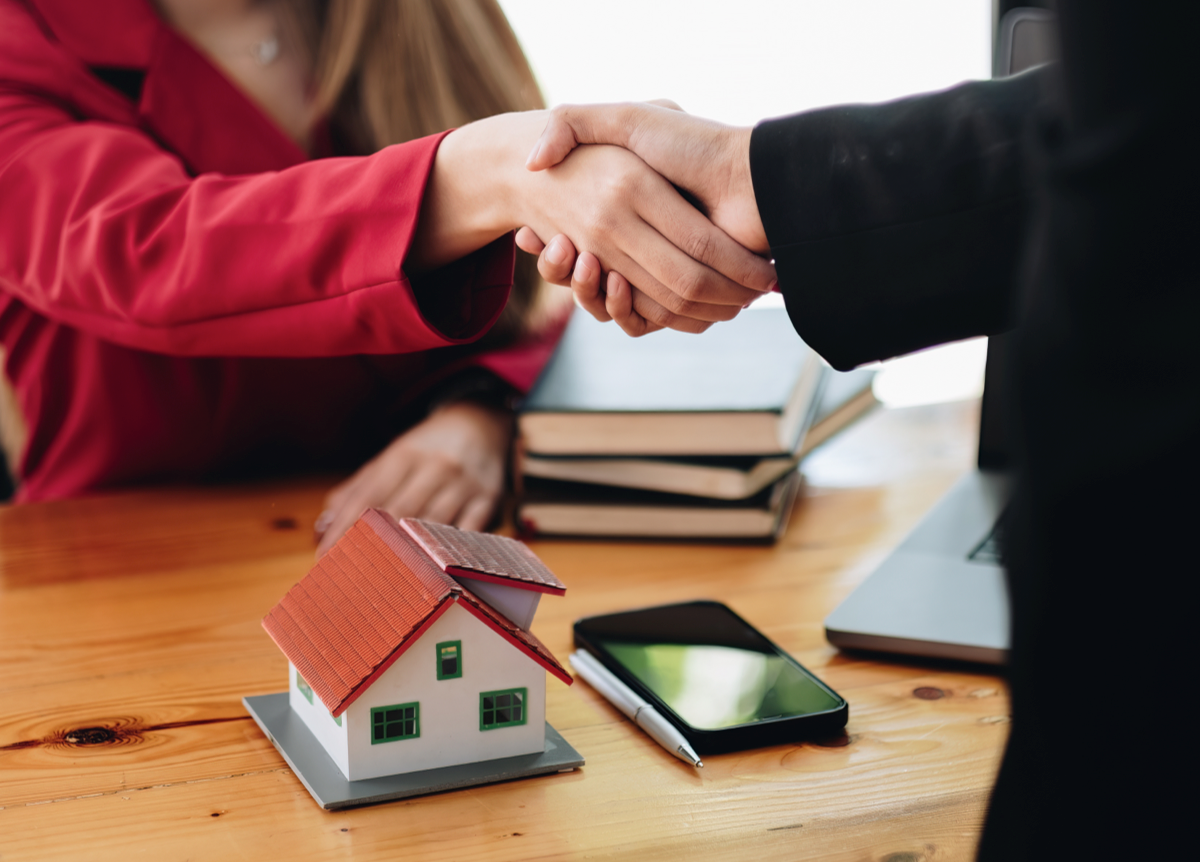 Man and woman shake hands above a model of a single-family home