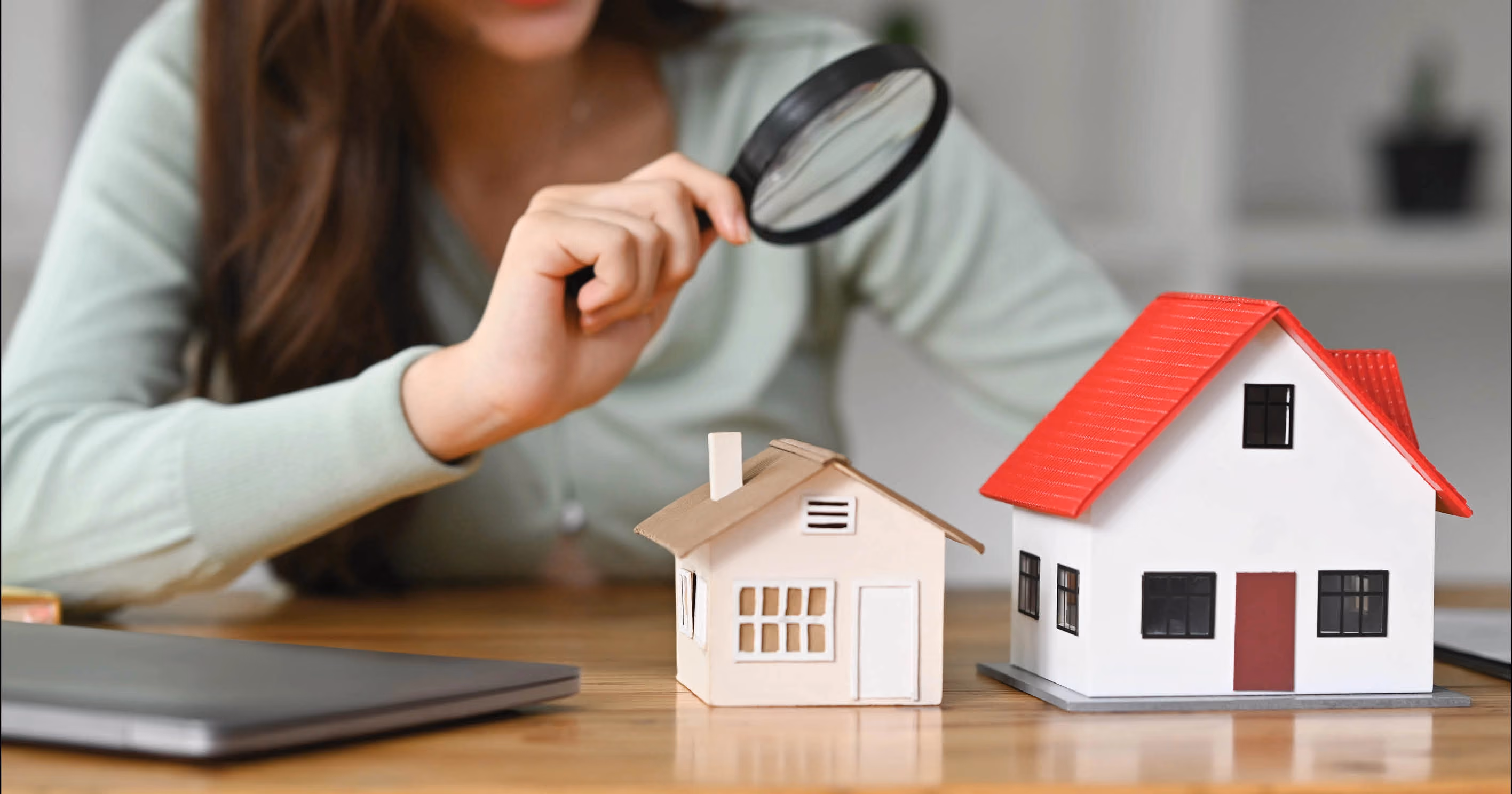 A woman looking at a model house through a magnifying glass