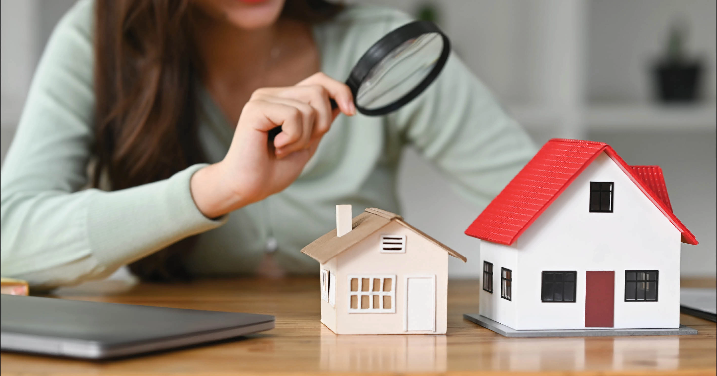 A woman looking at a model house through a magnifying glass