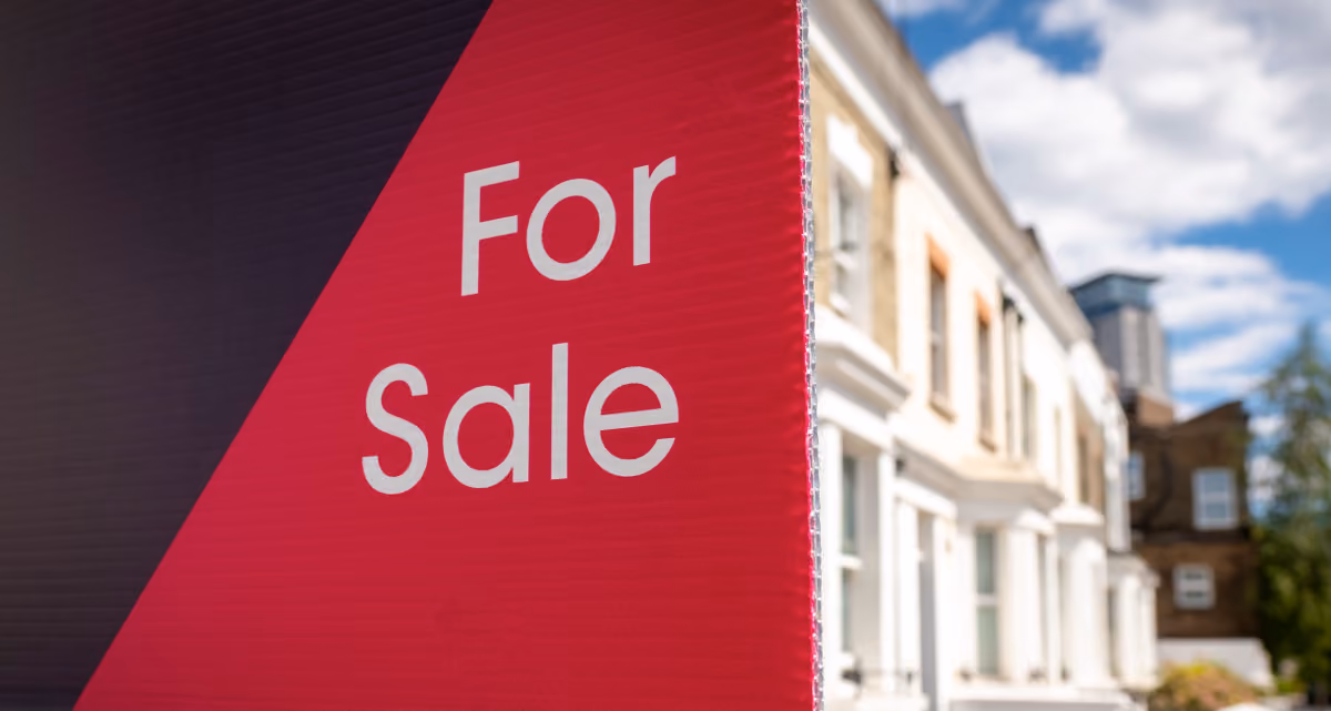 A For Sale sign next to a row of white terraced houses