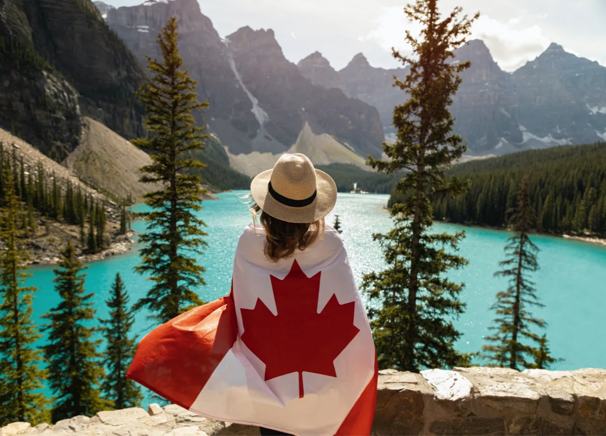 Woman draped in Canadian flag standing in front of Moraine Lake in Alberta