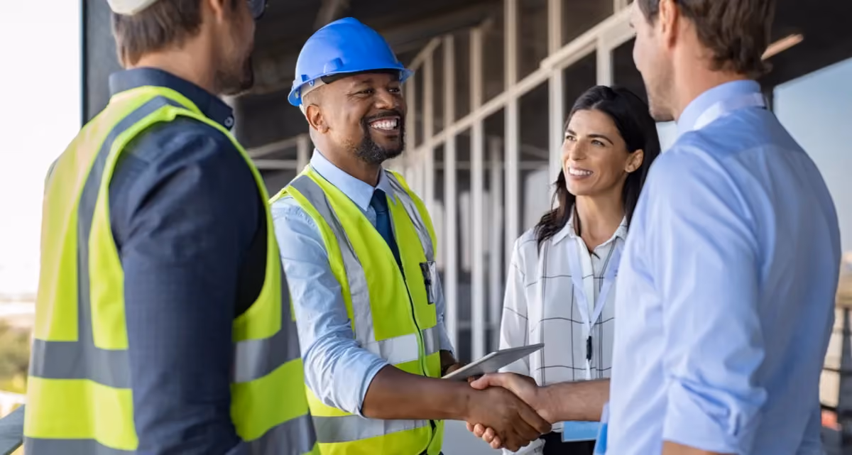 A man in a hard hat and high visibility jacket shakes hands with a man in business clothing