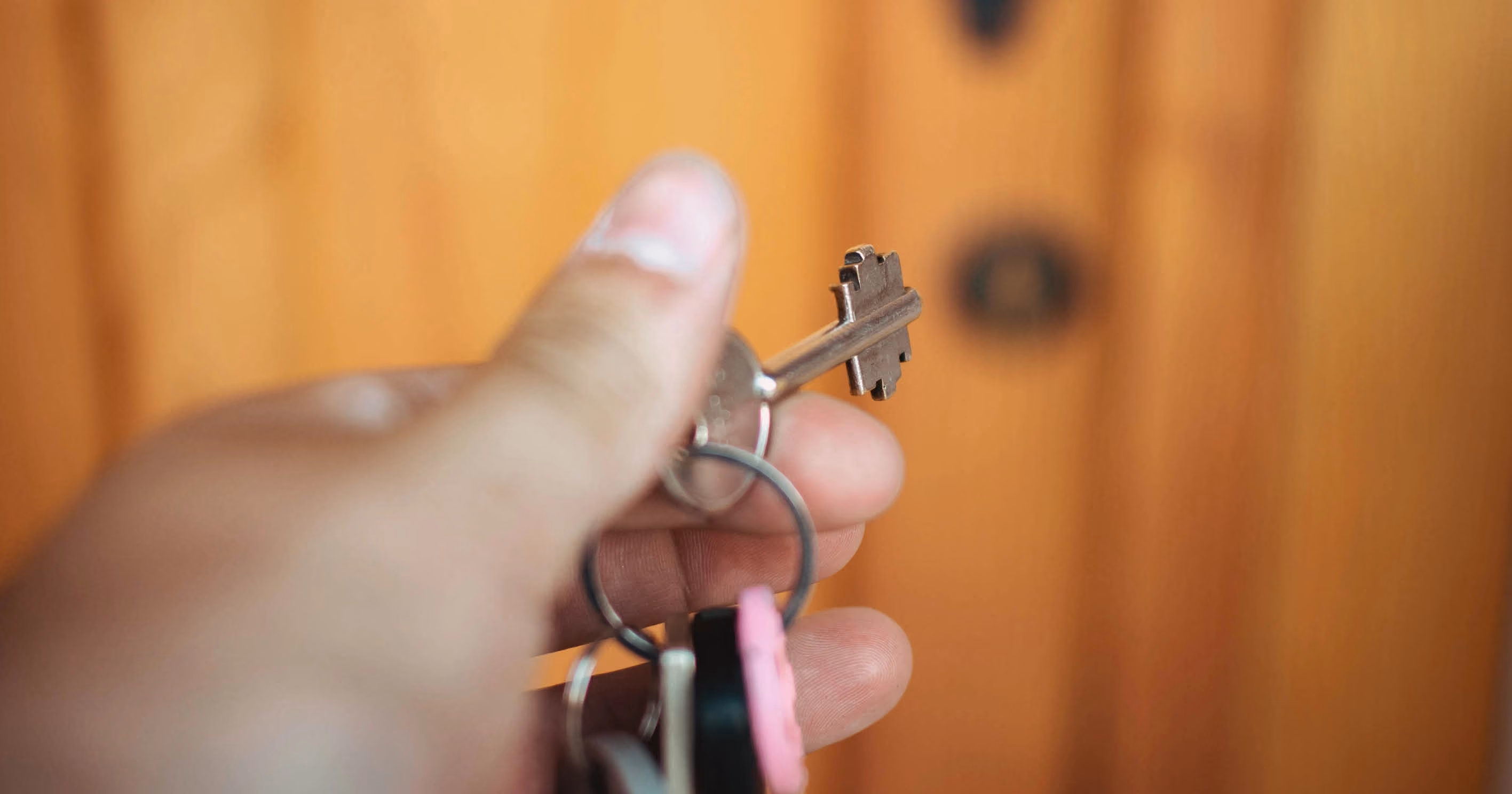 A hand holding a key reaching towards a door