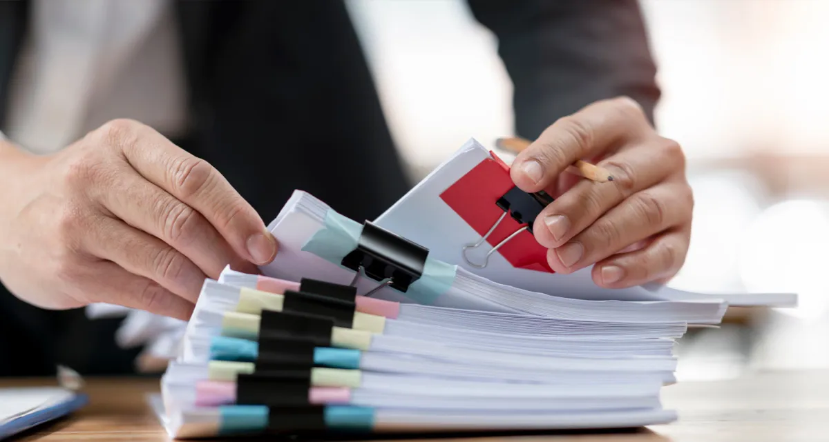 A man sorting through a stack of binder clipped documents