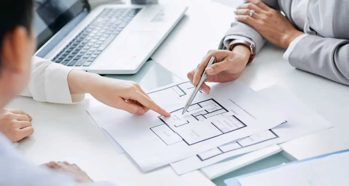 A house blueprint on a table with two people pointing at it