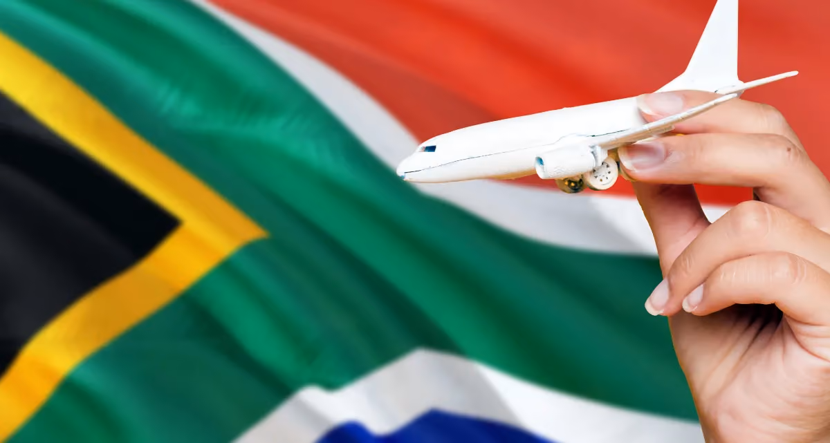 A hand holding up a model aeroplane in front of the South African flag