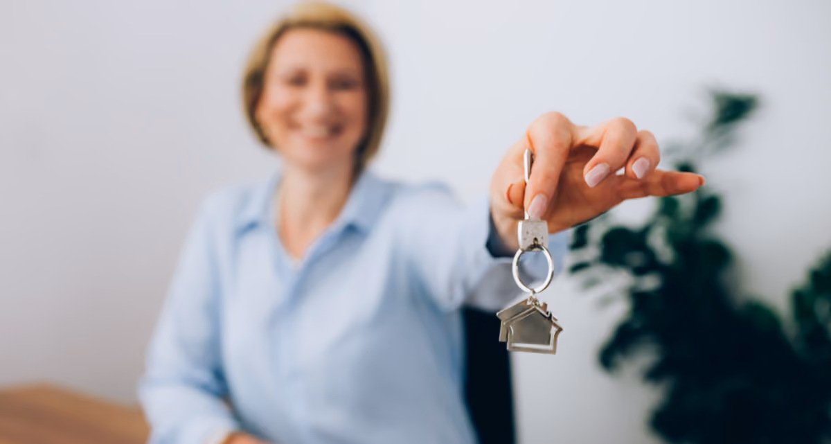 A woman holding up a set of keys with a house-shaped keyring