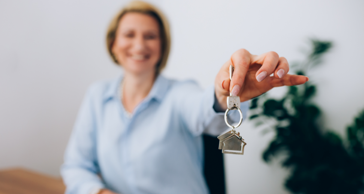 A woman holding up a set of keys with a house-shaped keyring