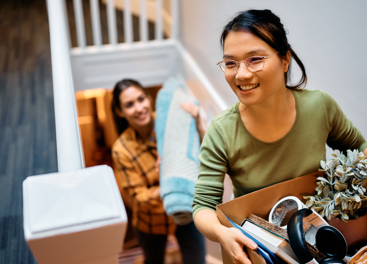 Two women carrying their belongings into a new apartment