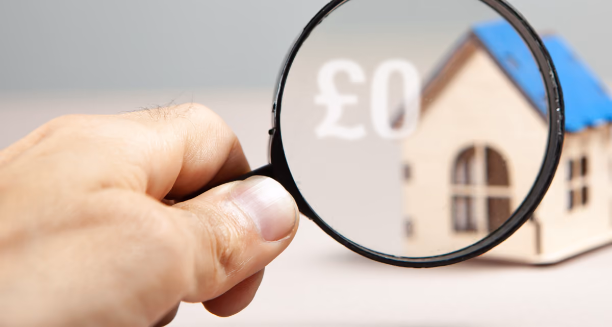 A hand holding up a magnifying glass in front of a model house