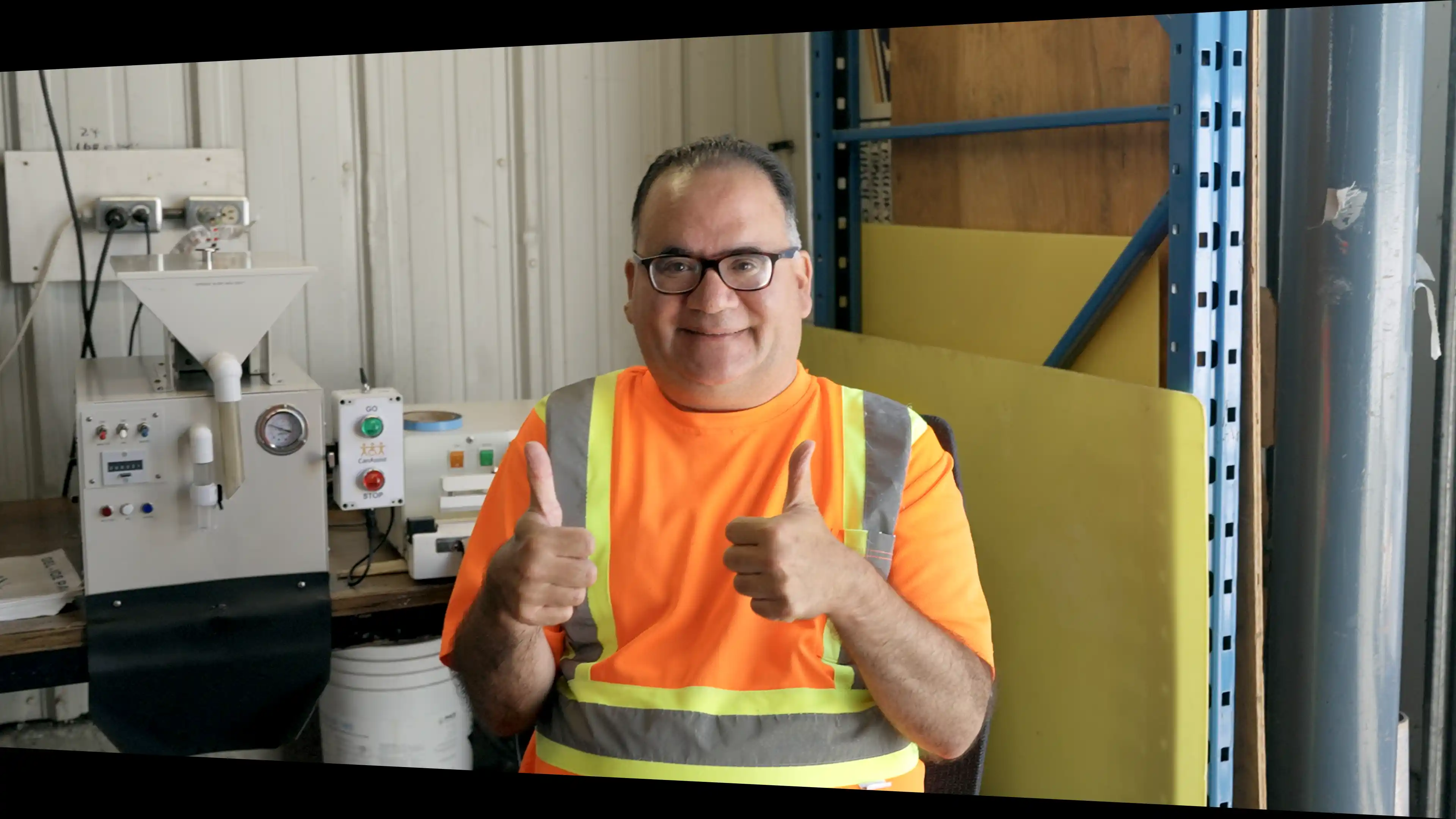 A CanAssist client at work, smiling with two thumbs up, in front of machinery augmented with CanAssist assistive technology