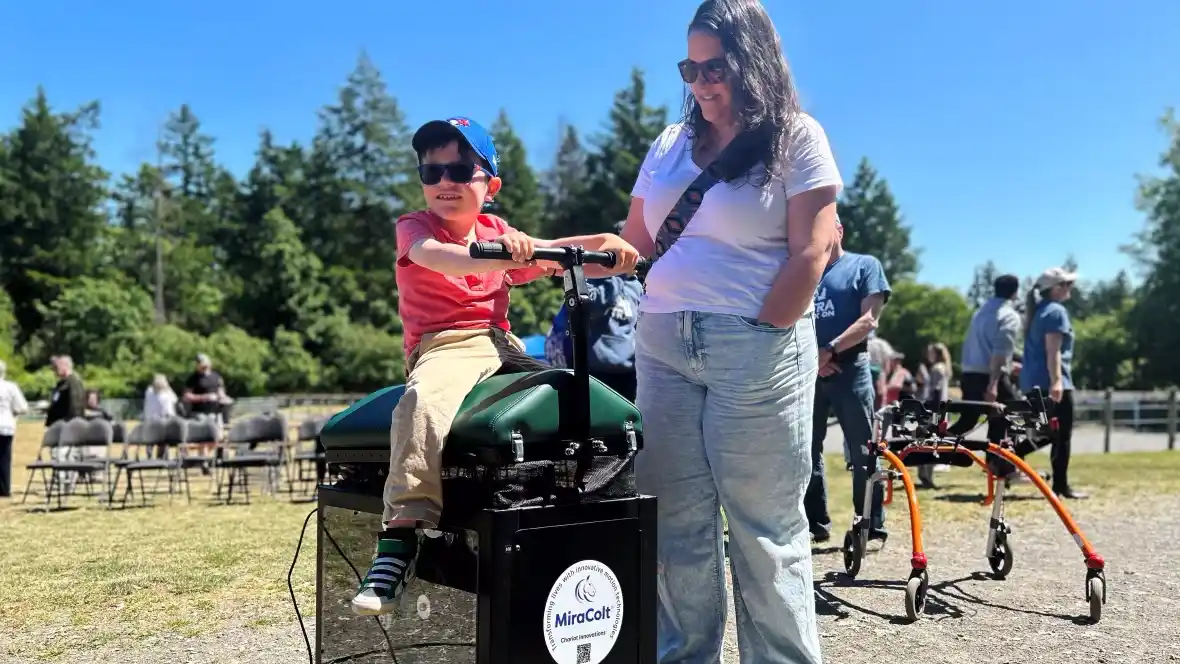 A child with their parent, enjoying CanAssist's horseback riding simulator