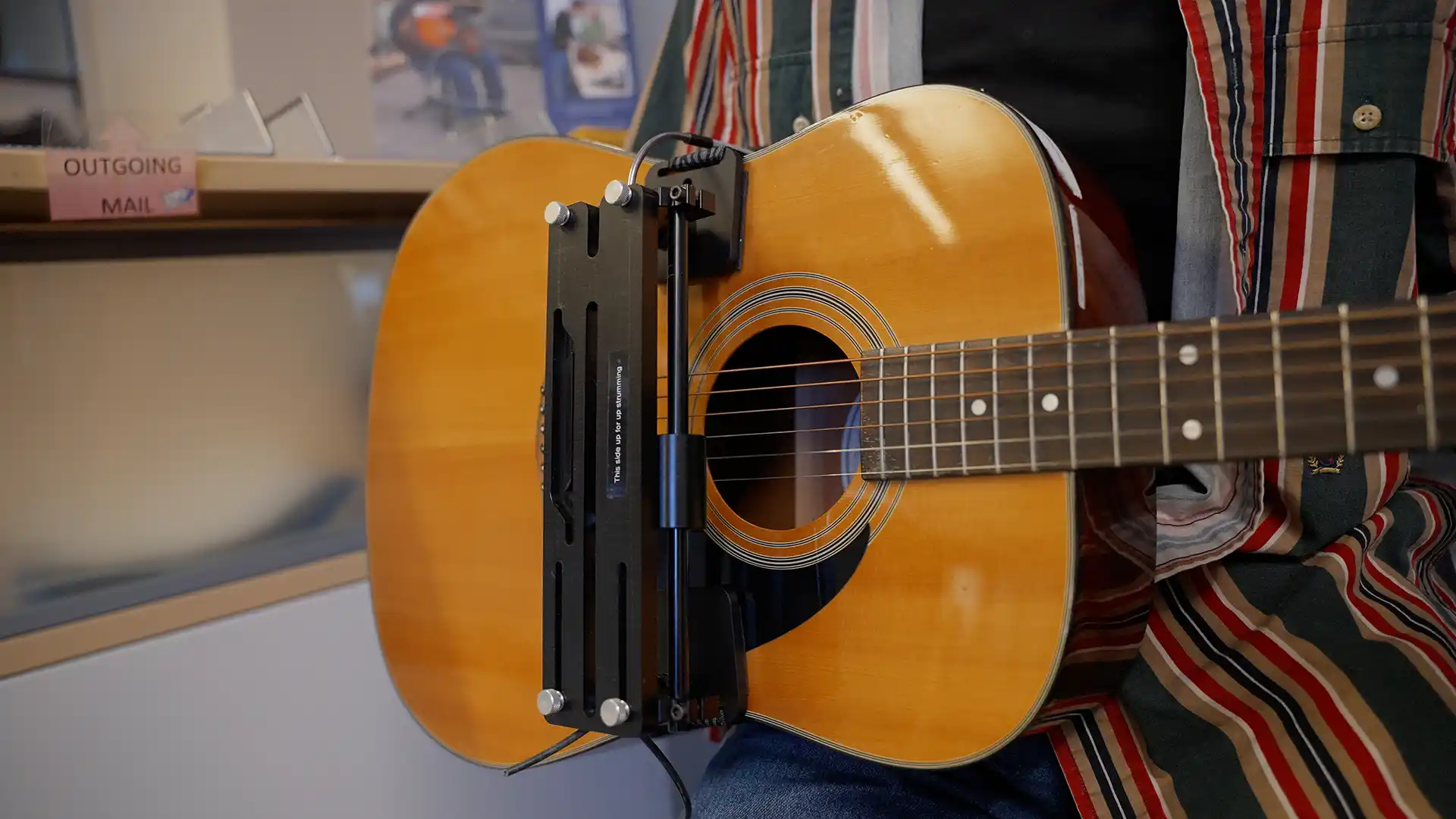 CanAssist's pedal-operated guitar strummer strapped over someone's shoulder