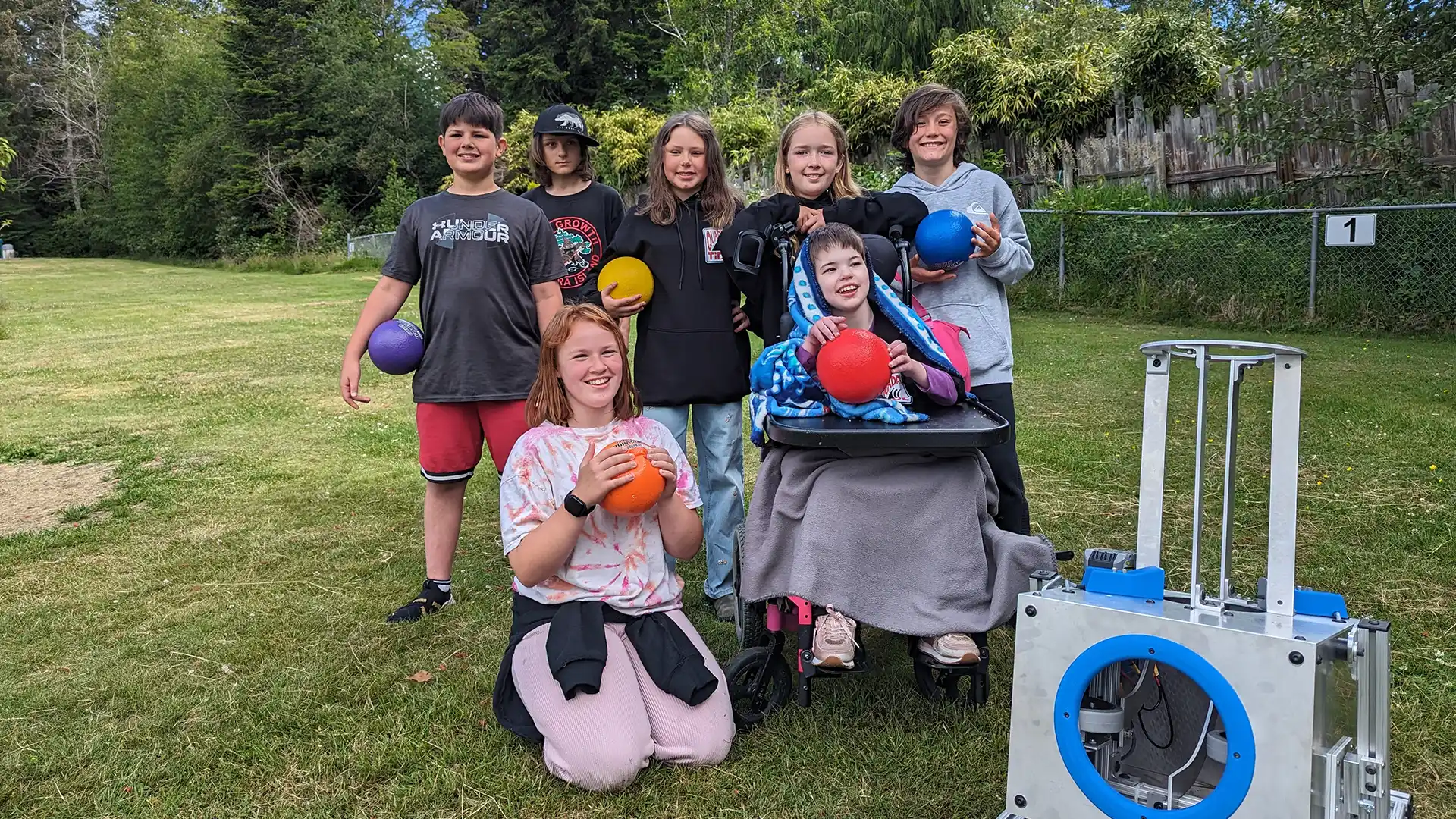 Smiling students gathered with dodgeballs and CanAssist's switch-accessible dodgeball launcher