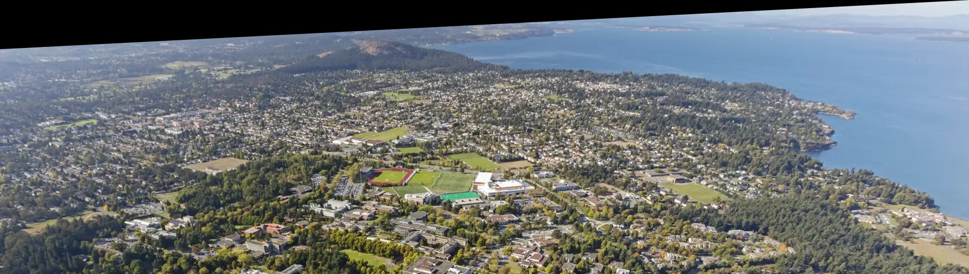 Aerial view of CanAssist's office at UVic, and the surrounding landscape full of trees, hills, and ocean