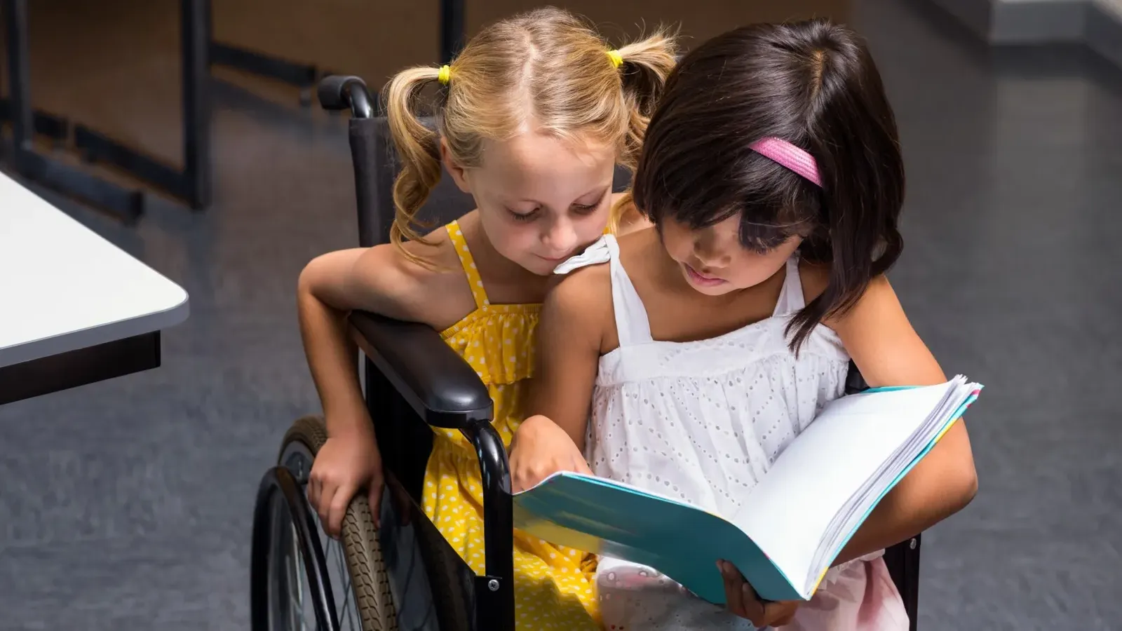 2 kids sitting in a wheelchair reading
