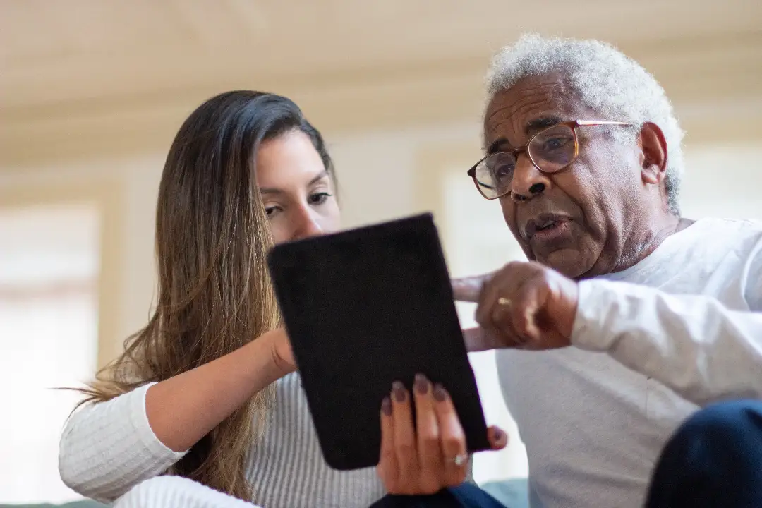 A student showing something on a tablet to a senior