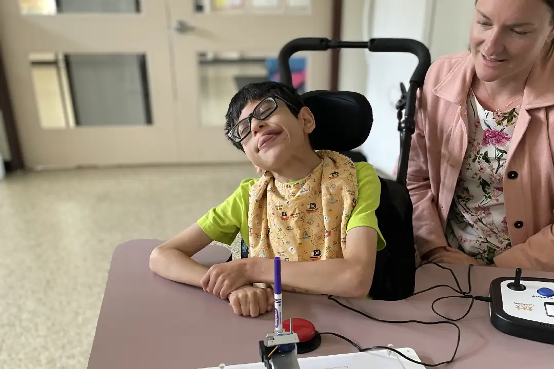 An adult sitting next to a child in a wheelchair using the switch-accessible art interface