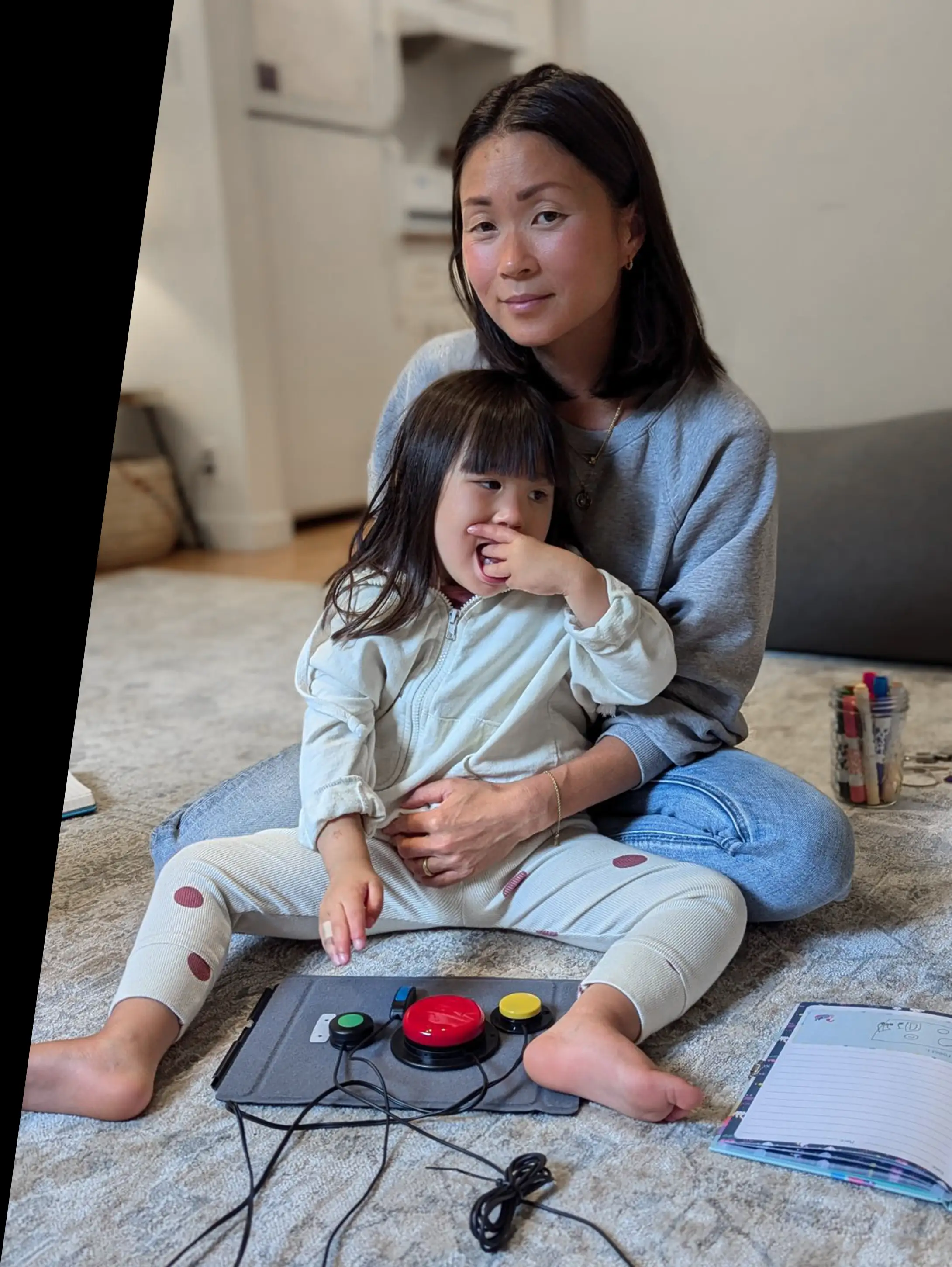 A mother and daughter sitting on a carpet in front of some switch-accessible assistive technology