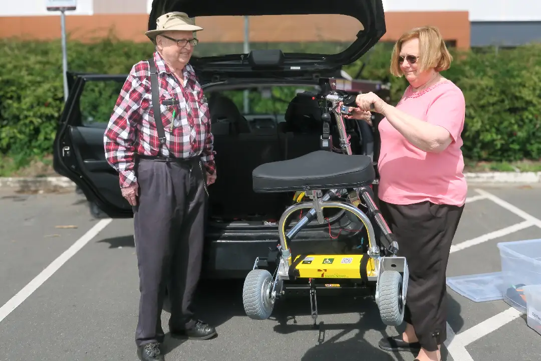 A couple standing at the back of a van with CanAssist's hitch lift lifting a mobility scooter into the trunk