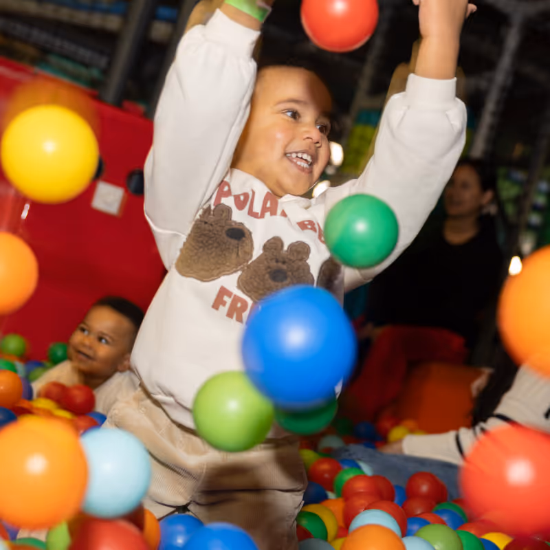 Joyful child playing in colorful ball pit with raised arms