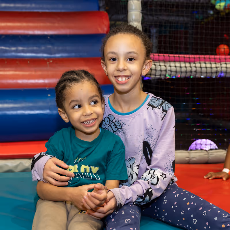 Two smiling children sitting together at colorful indoor playground