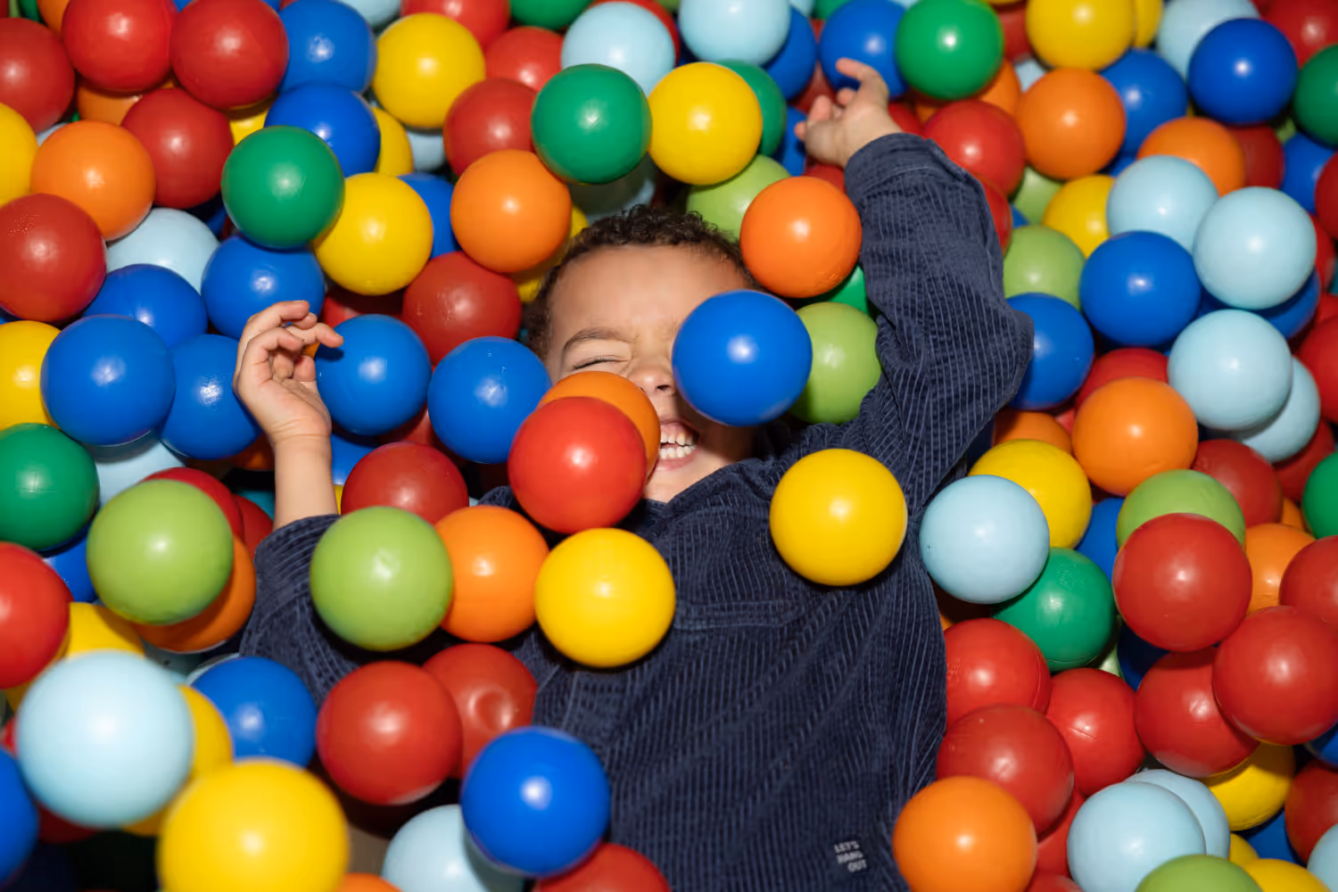 A boy smiling in a ball pool having lots of fun