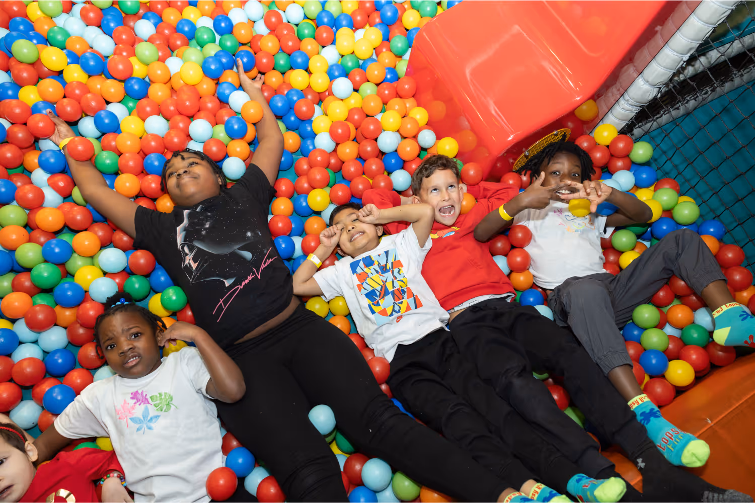 Boys lying down in a ball pool pulling faces and having fun