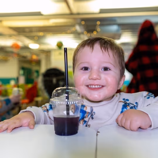 Smiling child with dark drink in cup at colorful indoor setting
