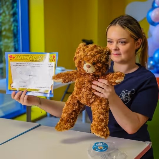 Woman holding fluffy teddy bear and certificate in colorful room