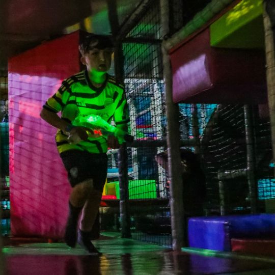 Player in neon green jersey holding laser tag  toy in dark arena