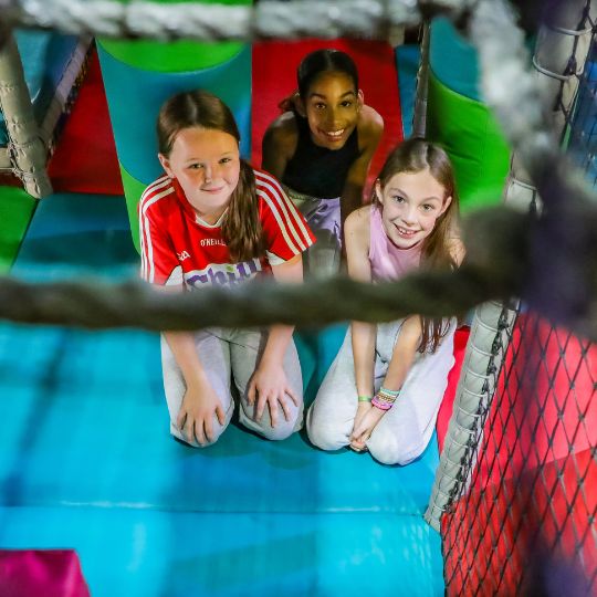 Three young girls smiling together on colorful play structure