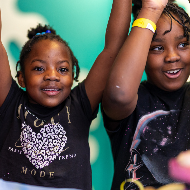 Two children smiling and raising their arms against teal background