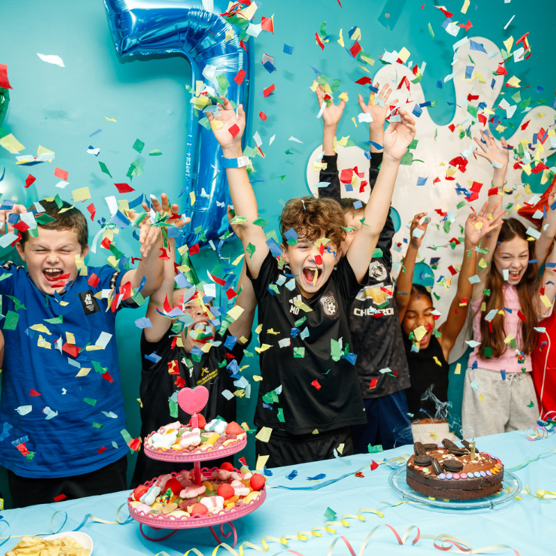 Kids celebrate with blue number one balloon, confetti, and birthday cakes
