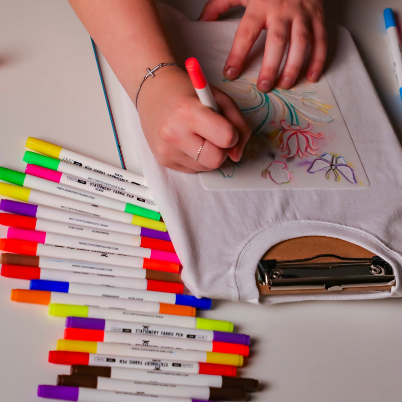 Colorful fabric markers drawing floral design on white surface