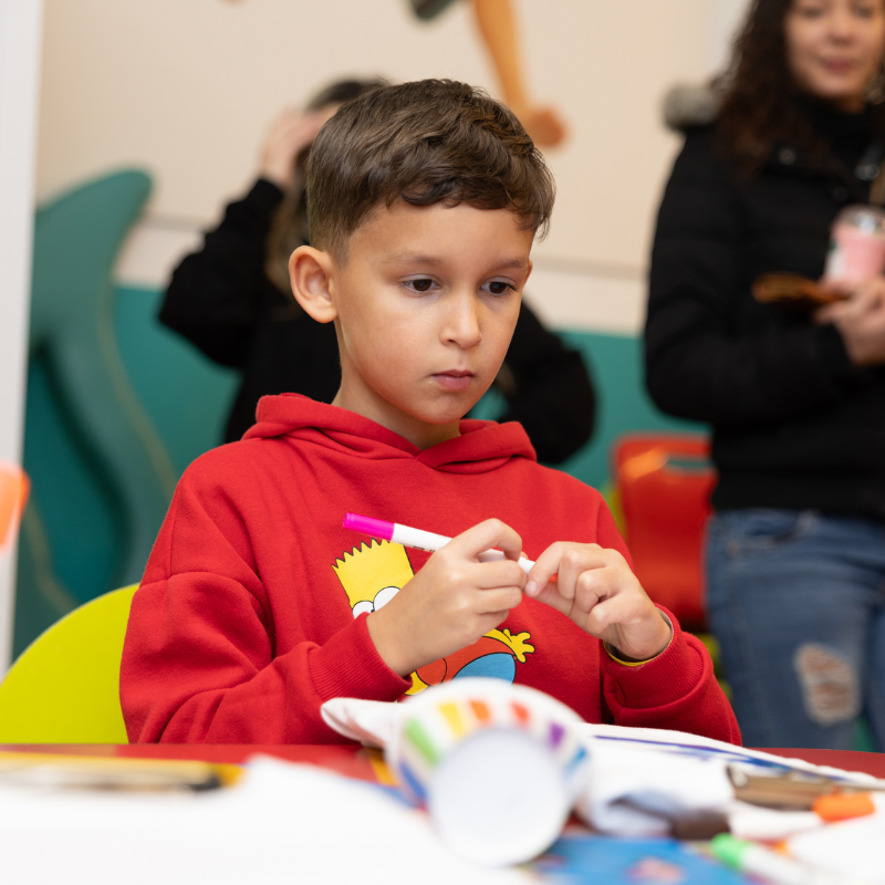 Child in red Bart Simpson hoodie concentrating on crafting activity
