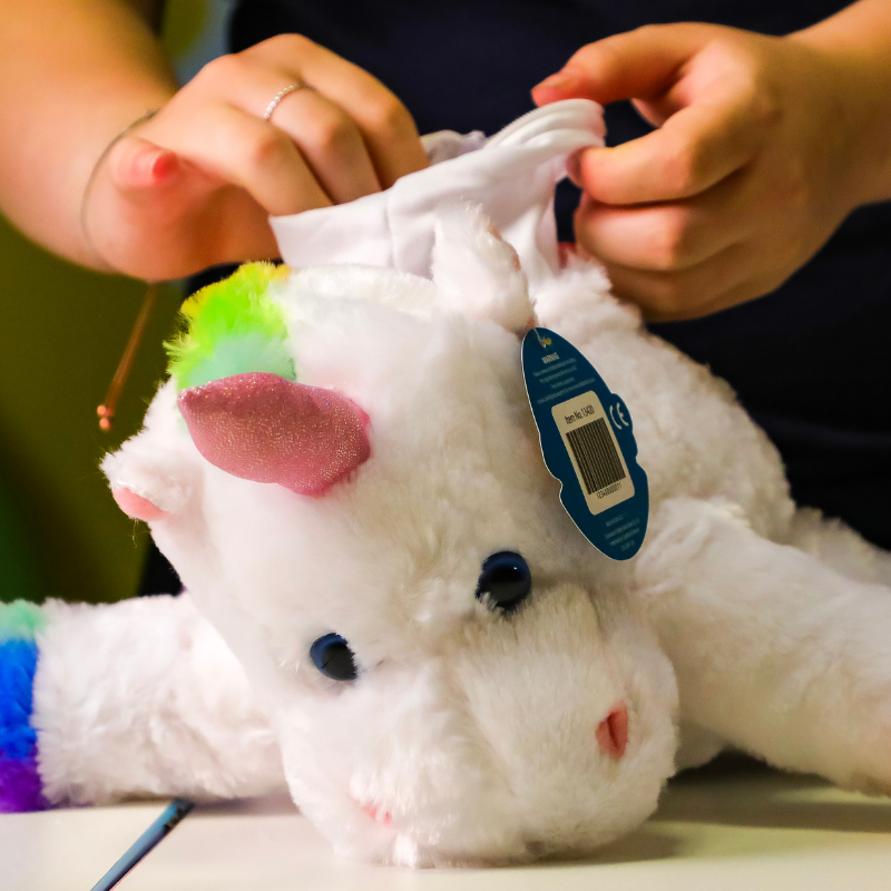 Hands fixing white plush unicorn with colorful mane and price tag