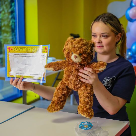 Woman holding fluffy teddy bear and certificate in colorful room