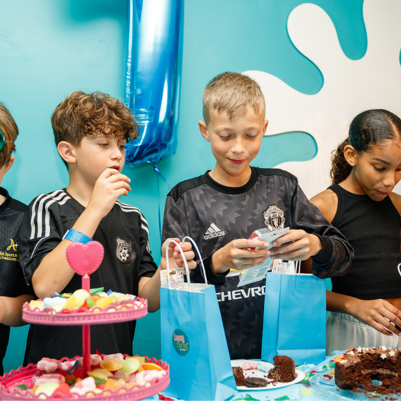 Children at birthday party with cake, gifts, and blue decorations
